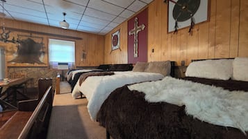 Et værelse med trævægge, et kors, et skjold, en stenvæg, en seng med et pelsdyne, en træbænk og en stenpejs.