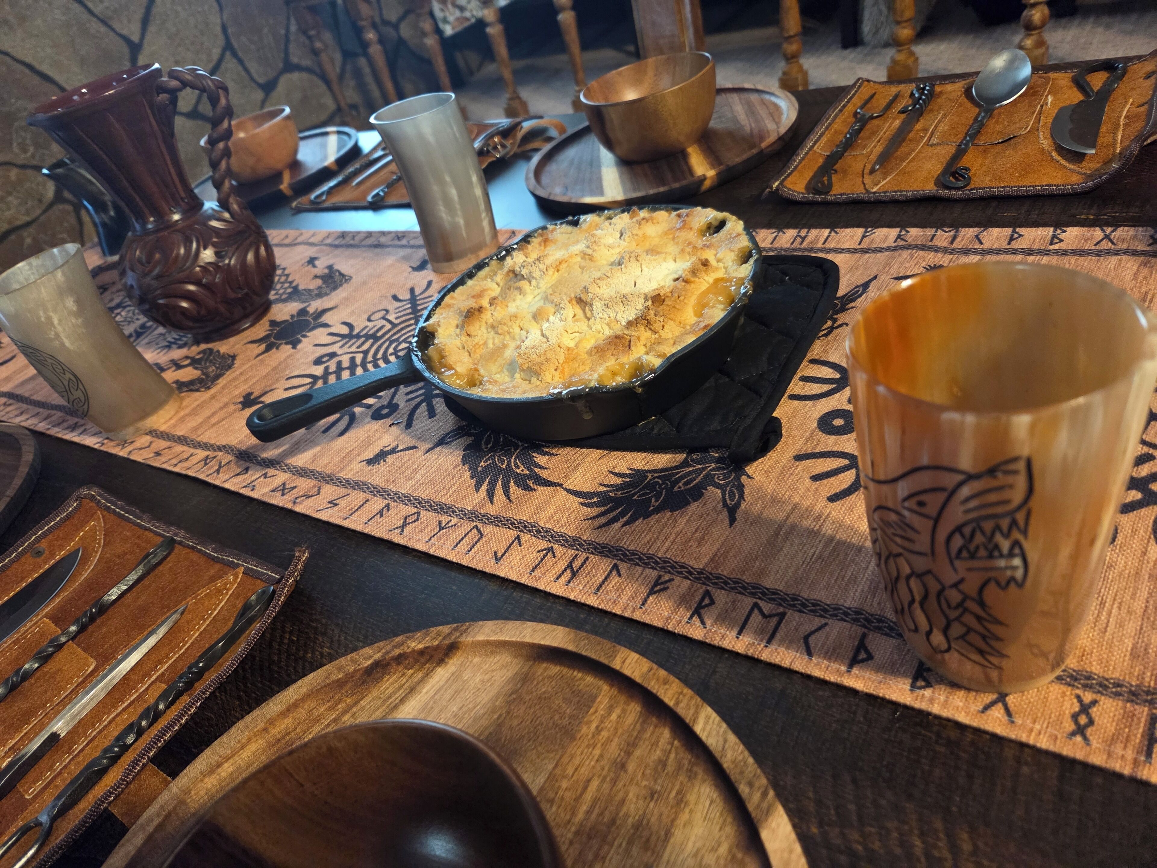 A rustic dining table with a pie, cutlery, and a woven placemat.
