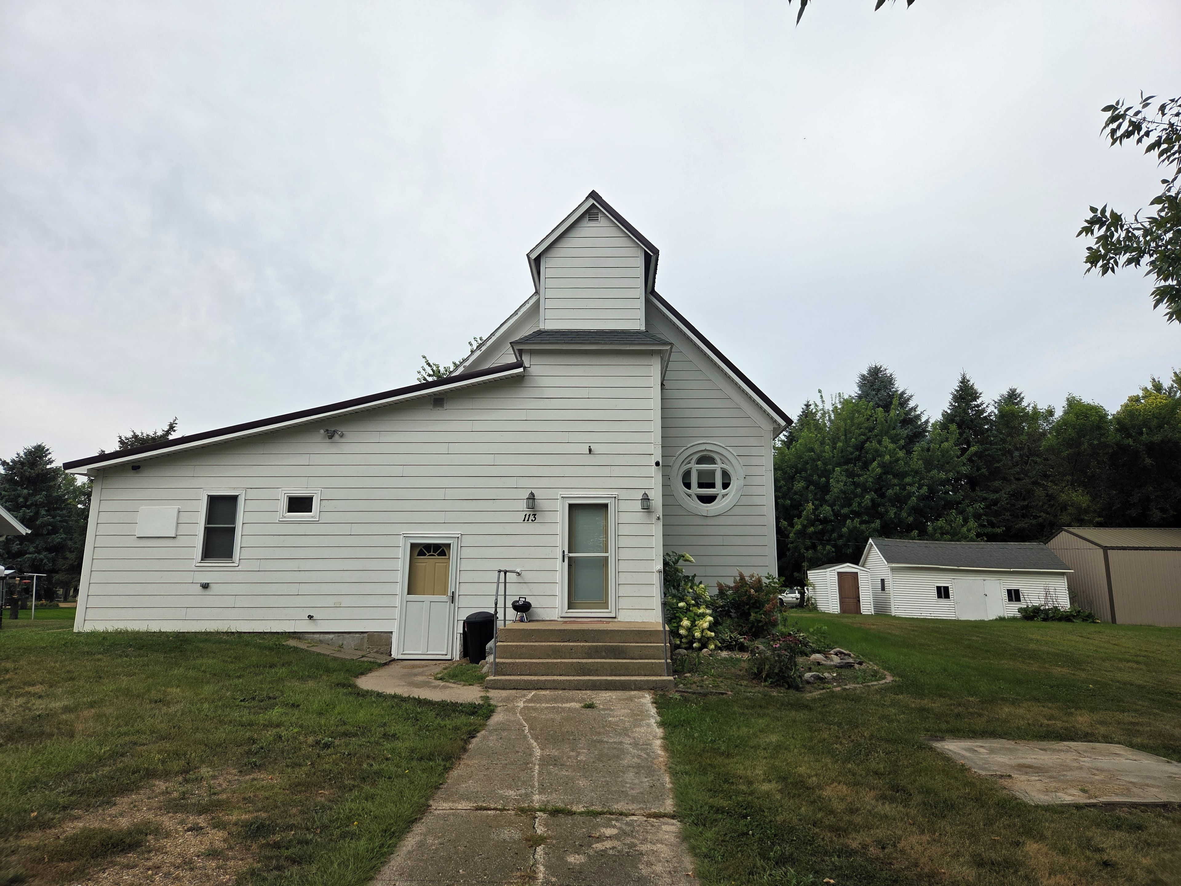 A white single-story building with a gabled roof, a front door, and a small circular window.