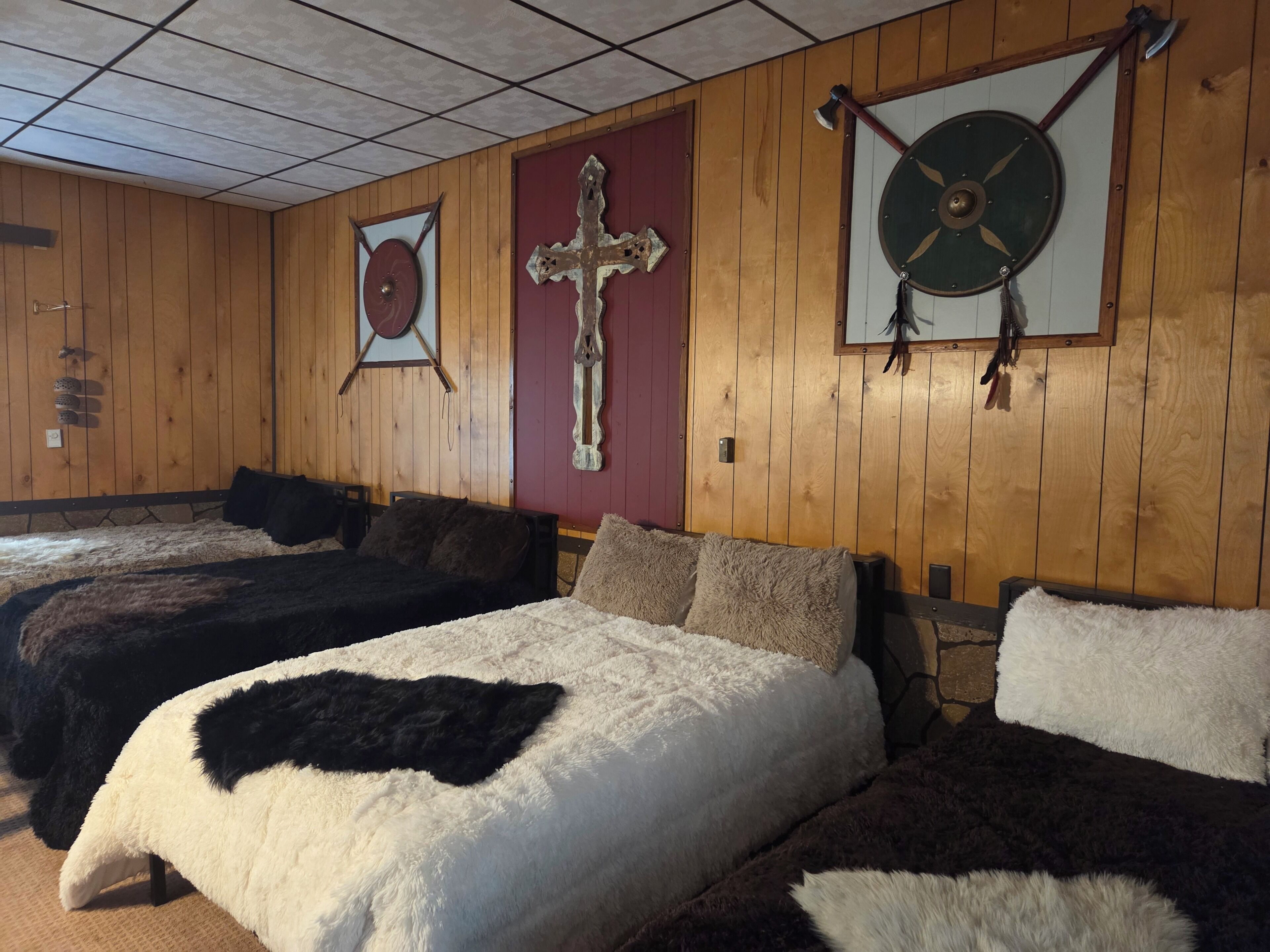 Une chambre avec deux lits, des murs en bois et une croix accrochée au mur.