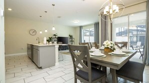 A modern kitchen with a central island, dining area with chairs and table set for four, and a large window providing natural light. - 4BR Storey Lake Resort Near Disney Private Pool (Kissimmee)