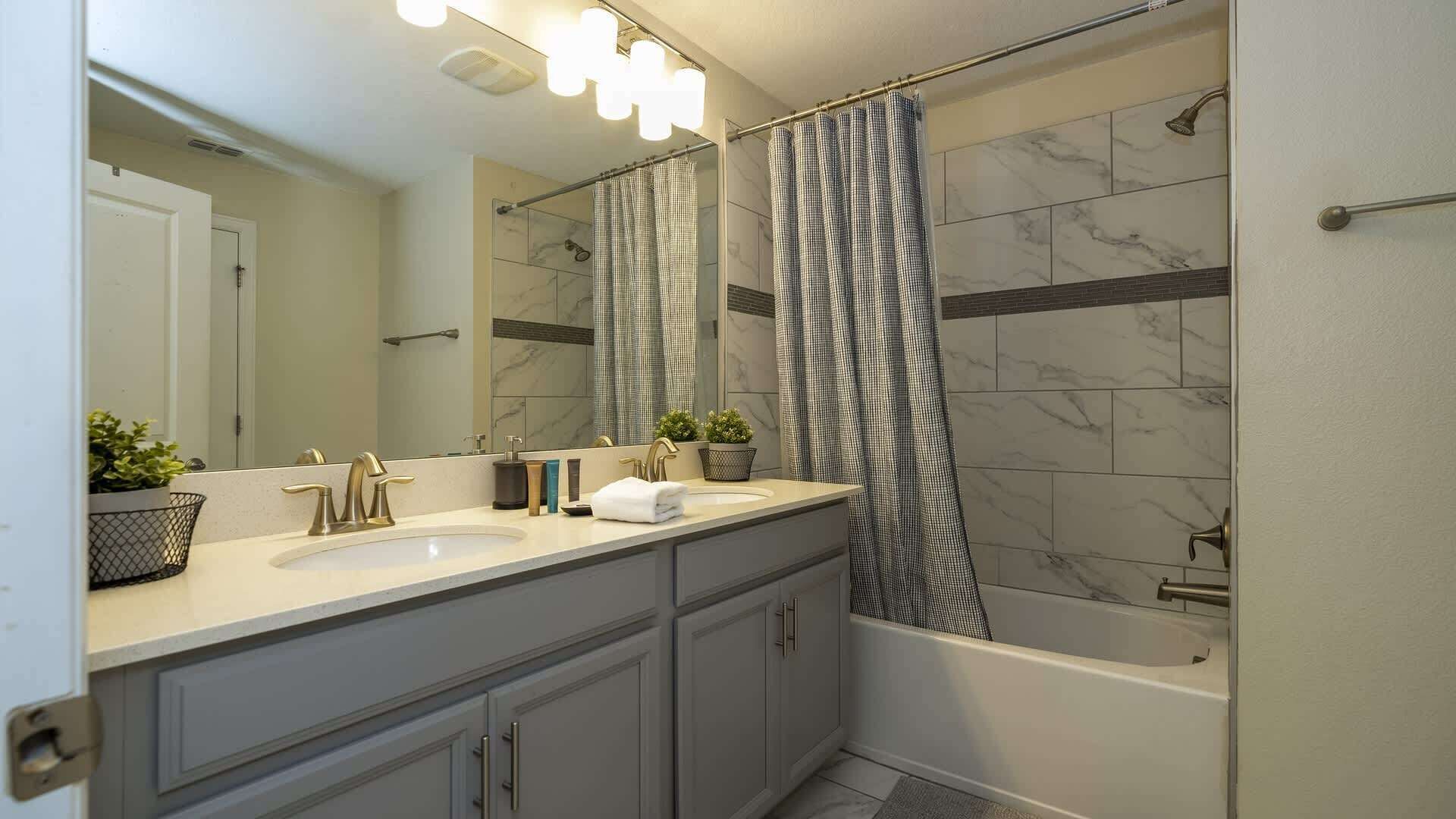 Un baño moderno con un lavamanos doble, un espejo grande, una ducha con cortina estampada y baldosas de mármol.