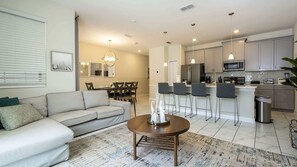 A modern living room with a sofa, a coffee table, and a dining area with chairs. - 4BR Storey Lake Resort Near Disney Private Pool (Kissimmee)