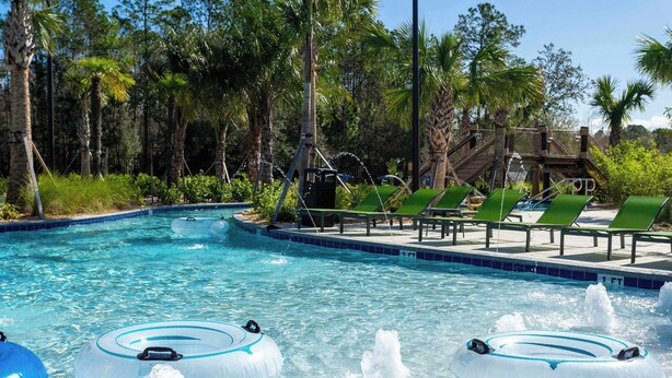 Una piscina con flotadores, sillas de descanso verdes y palmeras.