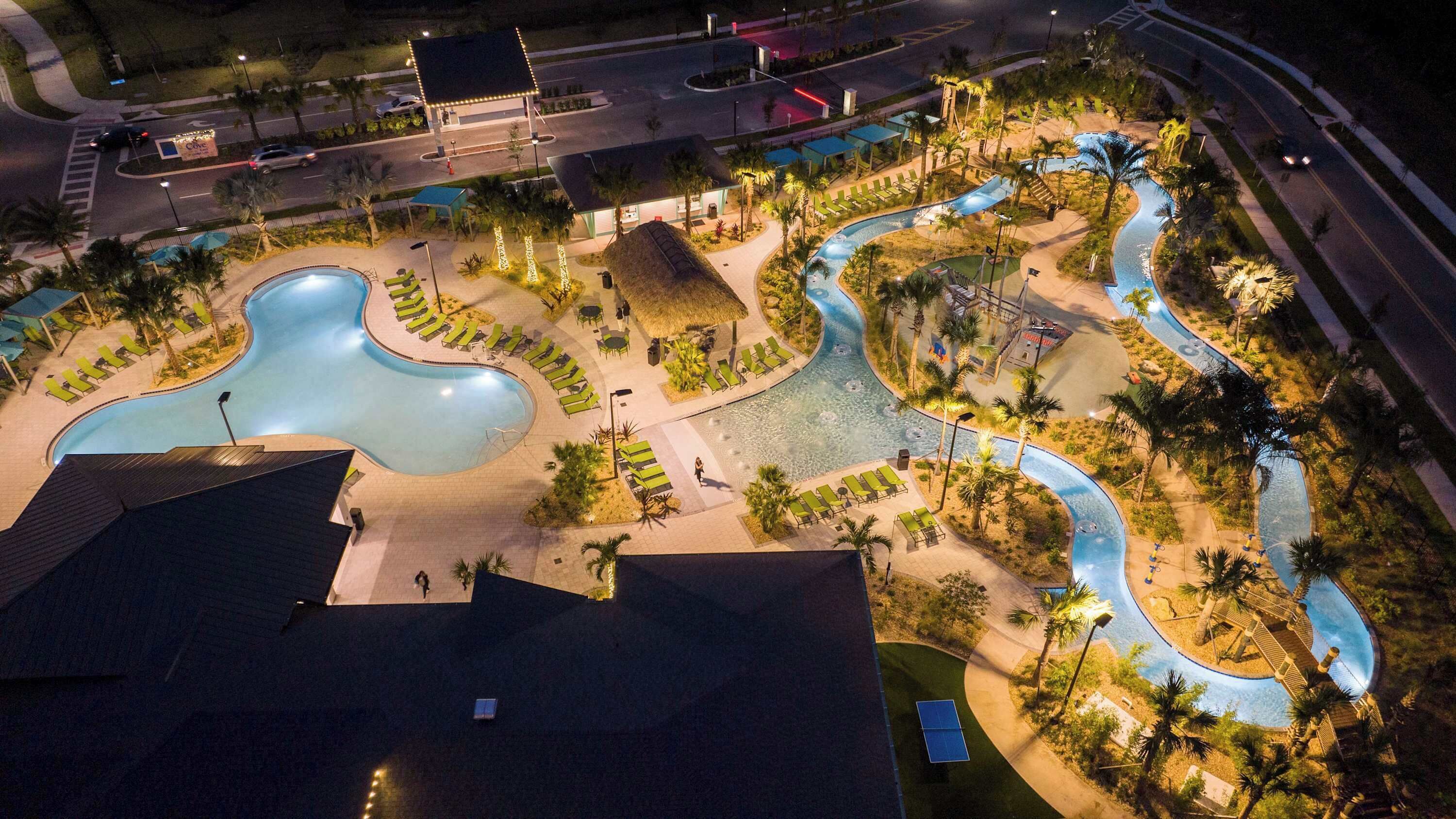 A swimming pool area with multiple pools and a water slide, surrounded by palm trees and lounge chairs.