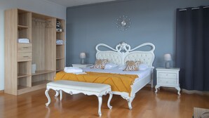 Un dormitorio con un armario grande, una cama con cabecero blanco, dos mesitas de noche y un reloj de pared.