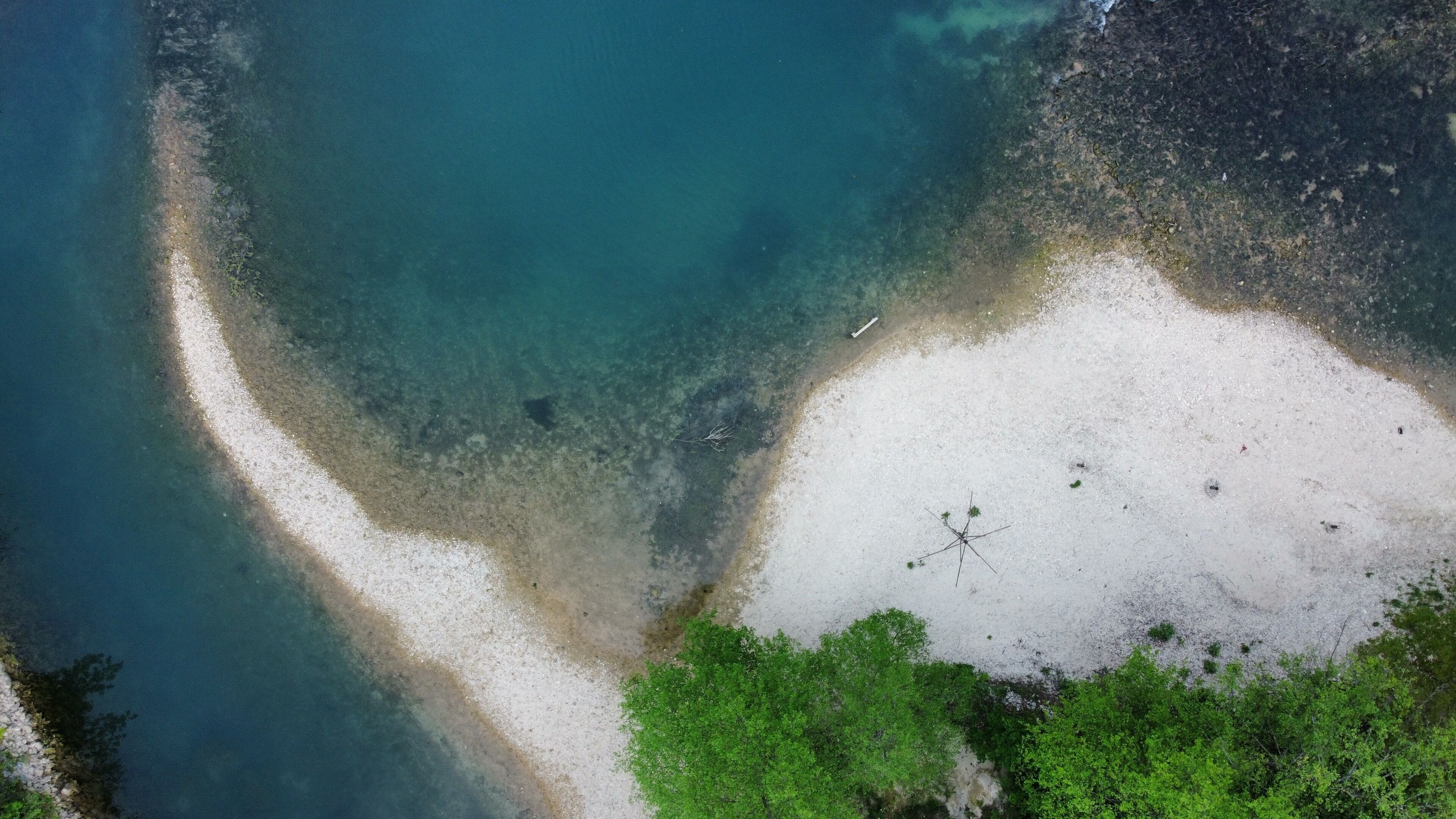 Vue aérienne d’une plage avec une eau cristalline, un rivage sablonneux et une végétation luxuriante qui borde le littoral.
