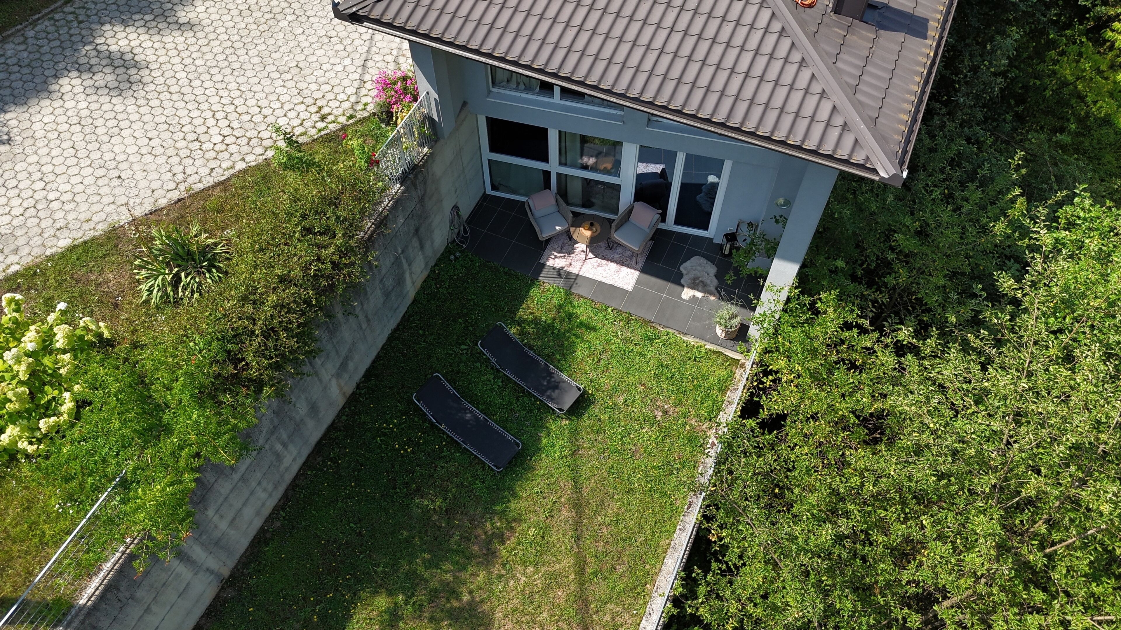 Une maison moderne avec un toit en tuiles, un petit patio avec deux fauteuils et une cour clôturée.