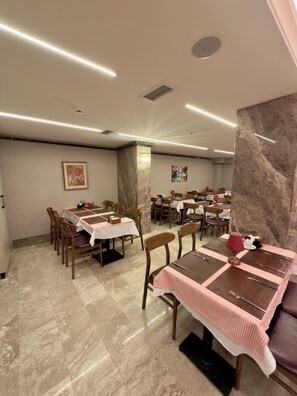 Zona pranzo con diversi tavoli e sedie, pavimento in marmo e luci a soffitto.
