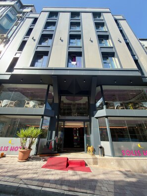 Entrada de hotel moderna con fachada de vidrio, alfombra roja y una planta en maceta.