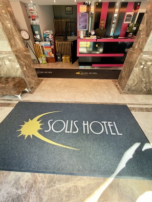 Un'area reception di un hotel, con la scrivania della reception, una sveglia e un cartello che indica il nome dell'hotel.