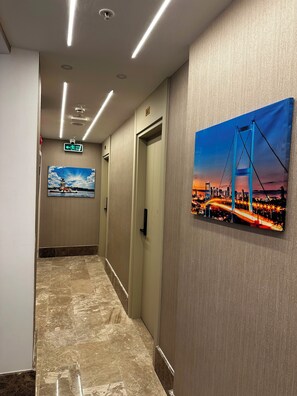 Un pasillo de hotel con suelo de mármol, techo con iluminación empotrada, señal de salida y un cuadro de un puente.