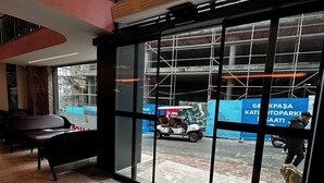 Entrada de un hotel con felpudo, mostrador de recepción y vista a la calle con obras.