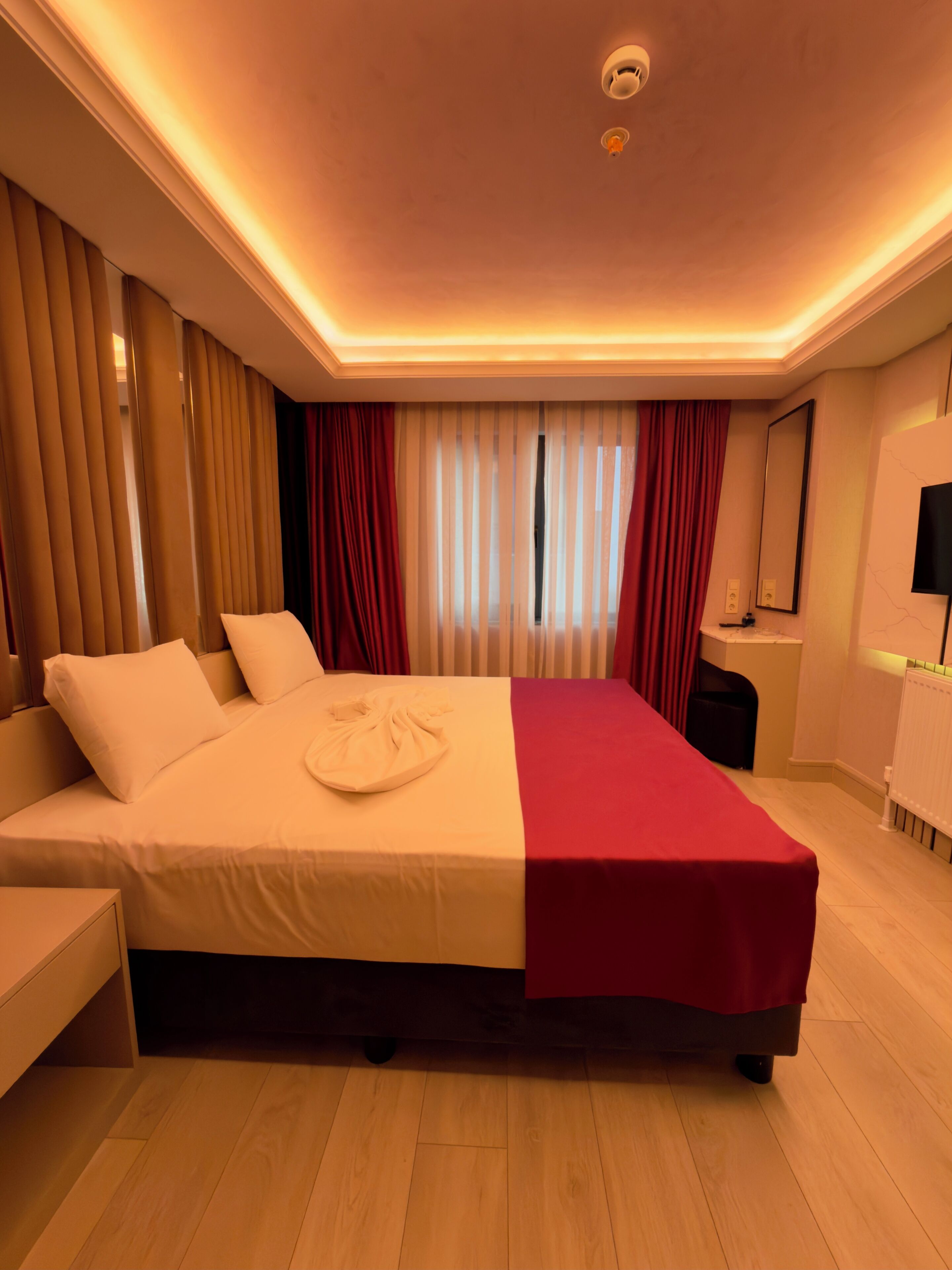 Habitación de hotel con una cama grande, una mesita de noche, un escritorio, una silla, un espejo y una ventana con cortinas.