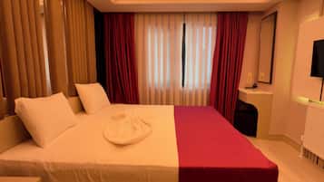 Habitación de hotel con una cama grande, una mesita de noche, un escritorio, una silla, un espejo y una ventana con cortinas.
