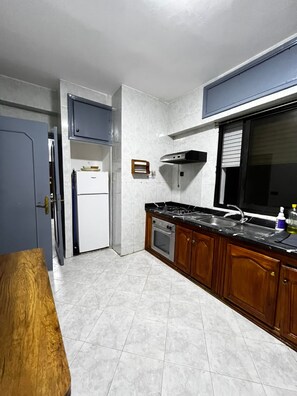 A compact kitchen with a refrigerator, stove, oven, and wooden cabinets. -  2-bedroom apartment in vibrant Tanger for your stay (Tanger)