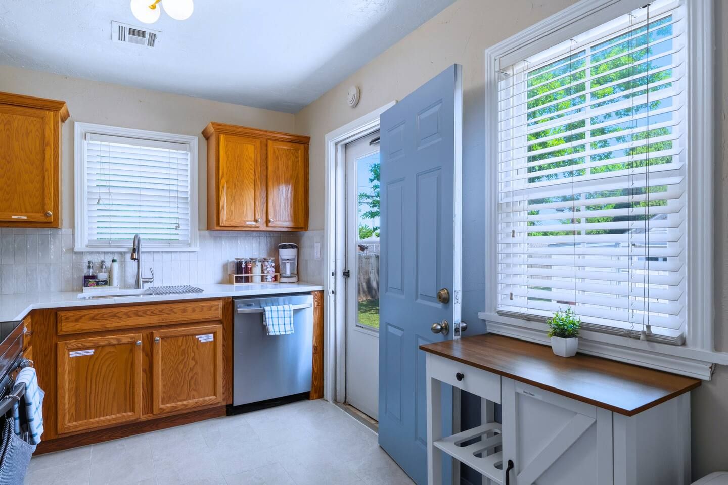 Una cocina con armarios de madera, lavavajillas y una ventana con persianas.