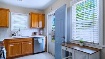 Una cocina con armarios de madera, lavavajillas y una ventana con persianas.
