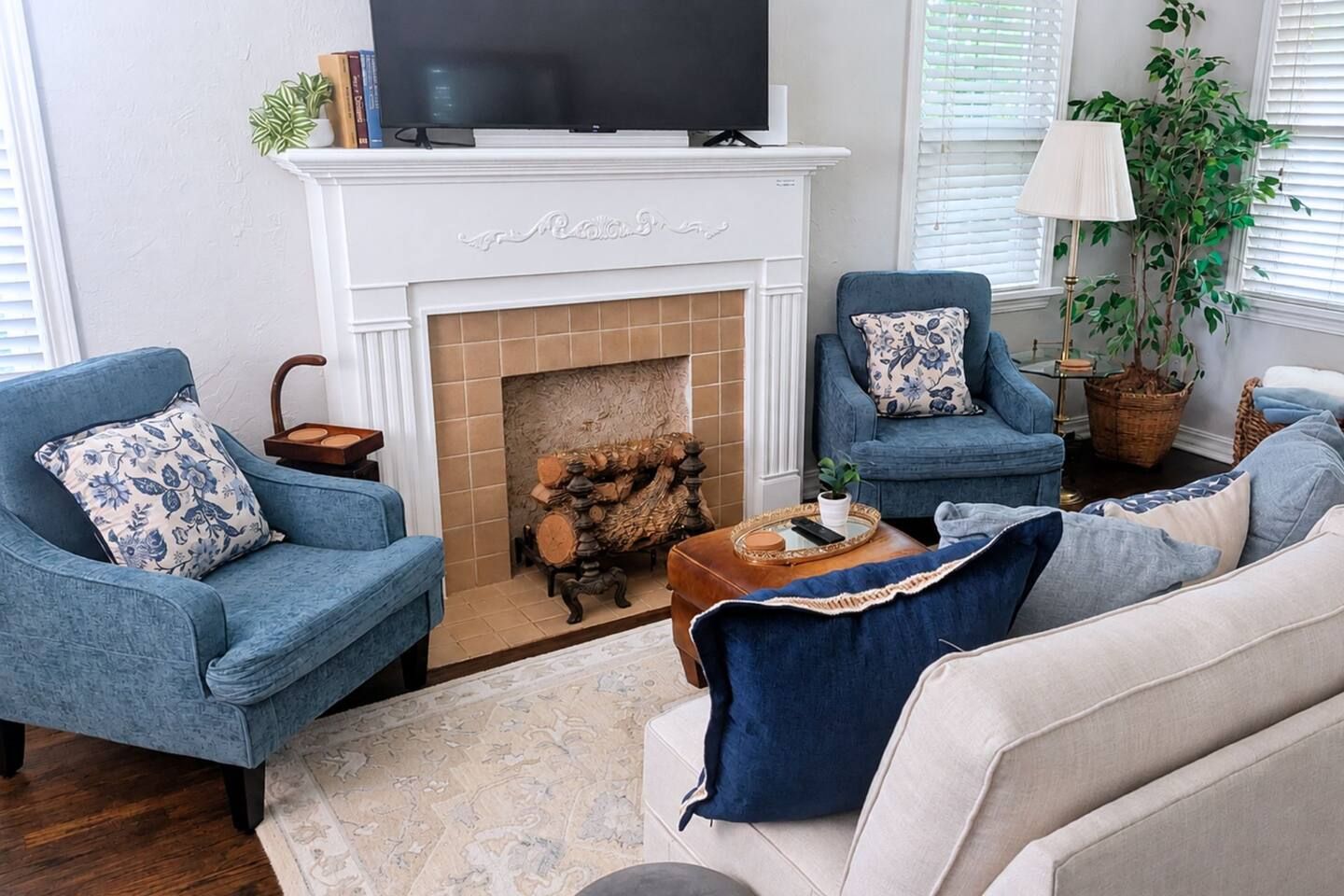 A living room with a fireplace, two blue armchairs, a sofa, and a television above the fireplace.