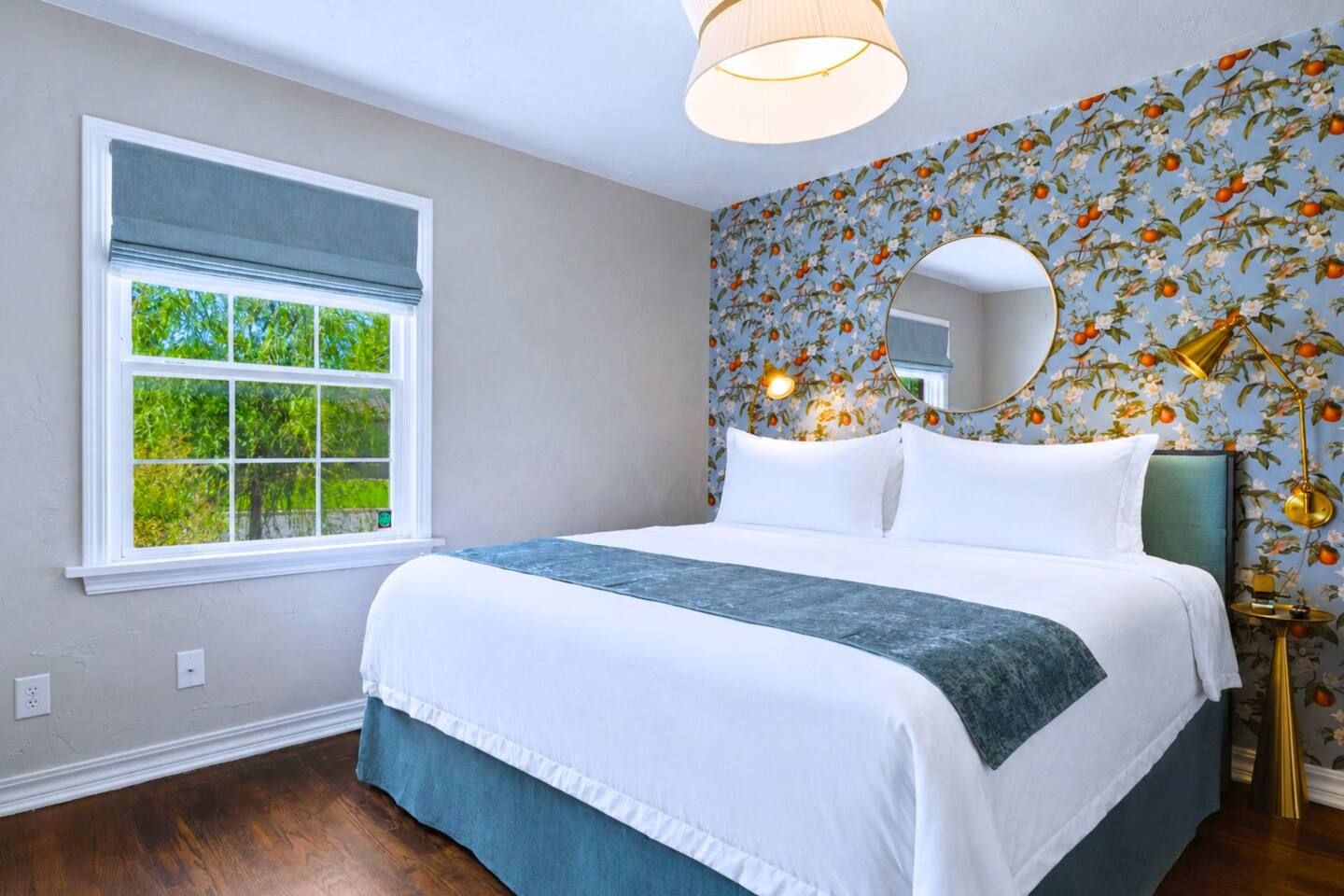 A bedroom with a large bed, a window with a view of greenery, and a floral wallpaper.