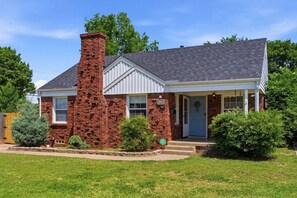 A two-story house with a brick chimney, white siding, and a front porch. - Clementine Cottage - By Fairgrounds, Kid-Friendly - Stay Smiley Rentals (Oklahoma City)