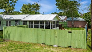 A house with a green fence, a covered porch, and a metal roof. - One More Cast Coastal House with Fenced Yard and Screened Porch near the Ocean (Fulton)