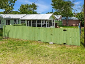 A house with a green fence, a covered porch, and a metal roof. - One More Cast Coastal House with Fenced Yard and Screened Porch near the Ocean (Fulton)