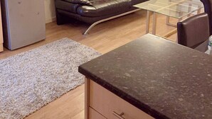 A compact living space with a kitchenette, a sofa, a glass-top table, and a refrigerator. - 2 Spacious Double Bedroom - Bradford City Center (Bradford)