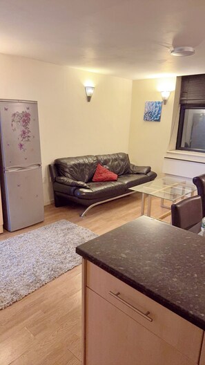 A compact living space with a kitchenette, a sofa, a glass-top table, and a refrigerator. - 2 Spacious Double Bedroom - Bradford City Center (Bradford)