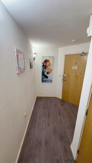 A hallway with a wooden door, a wall-mounted light fixture, and a framed artwork. - 2 Spacious Double Bedroom - Bradford City Center (Bradford)