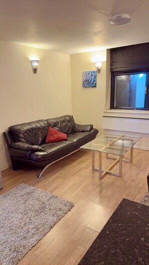 A living room with a leather sofa, a glass coffee table, a rug, and a painting on the wall. - 2 Spacious Double Bedroom - Bradford City Center (Bradford)