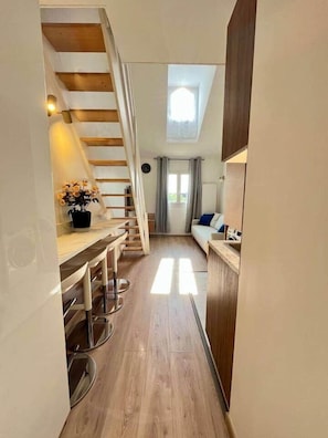 Un corridoio stretto con una scala in legno che conduce a una camera da letto soppalcata, una piccola cucina e un angolo salotto con vista sull'esterno.