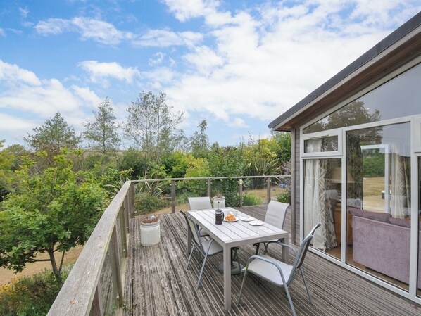 A wooden deck with a table and chairs, overlooking a garden and a building with large windows.