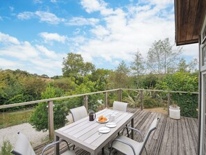 An outdoor dining area with a table set for two, surrounded by chairs, on a wooden deck with a view of a natural landscape.