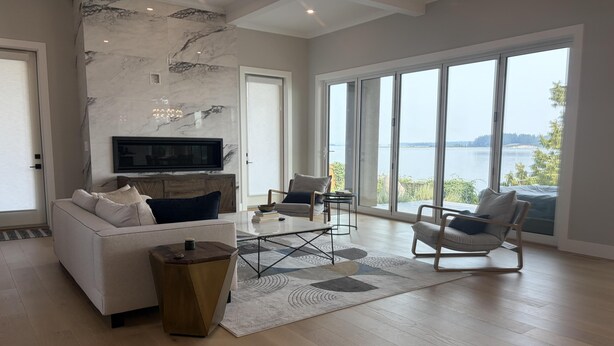 A spacious living room with a large window, a sofa, a coffee table, and a television. - Coastal Elegance and Oceanfront Luxury Estate (Central Saanich)