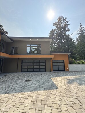 Une maison moderne à deux étages, dotée d’un grand garage et d’une allée pavée.