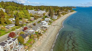 A coastal residential area with houses, a beach, and a forested hillside. - Coastal Elegance and Oceanfront Luxury Estate (Central Saanich)