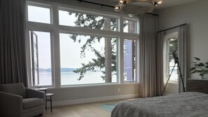 A bedroom with a large window, a bed, a chair, and a small table. - Coastal Elegance and Oceanfront Luxury Estate (Central Saanich)