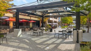 An outdoor patio area with tables and chairs, covered by a glass and metal structure. - Coastal Elegance and Oceanfront Luxury Estate (Central Saanich)