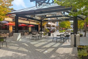 Un espace extérieur aménagé en terrasse, avec des tables et des chaises, et recouvert d’une structure en verre et en métal.