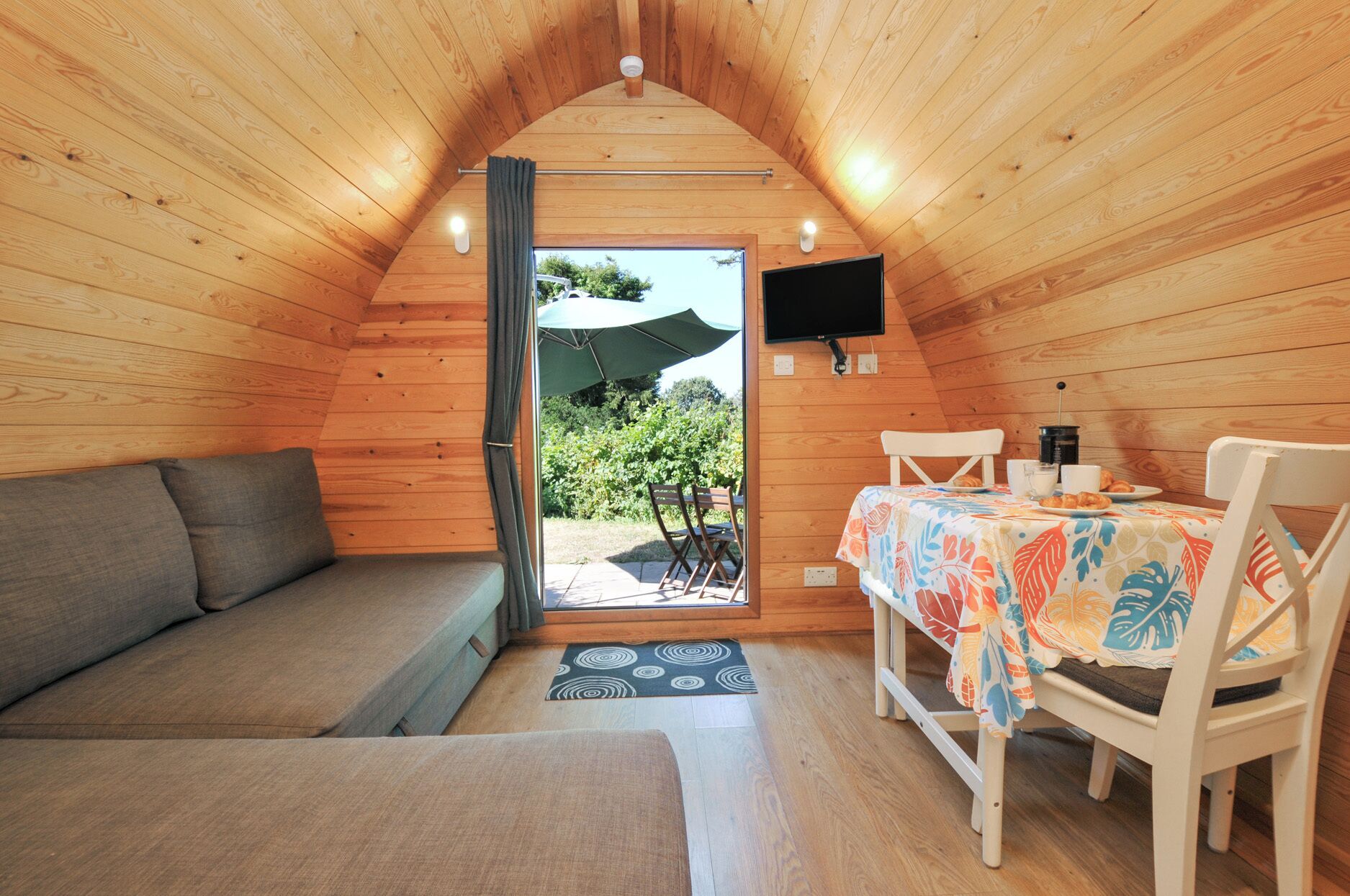 Ein gemütliches Zimmer mit Holzbalkendecke, einer Couch, einem Esstisch mit Stühlen und einem an der Wand befestigten Fernseher.