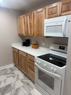 A kitchen with wooden cabinets, a white microwave, a black coffee maker, and a white stove. - The Milk House No. 1- Farm life at its Best! (Bidwell)