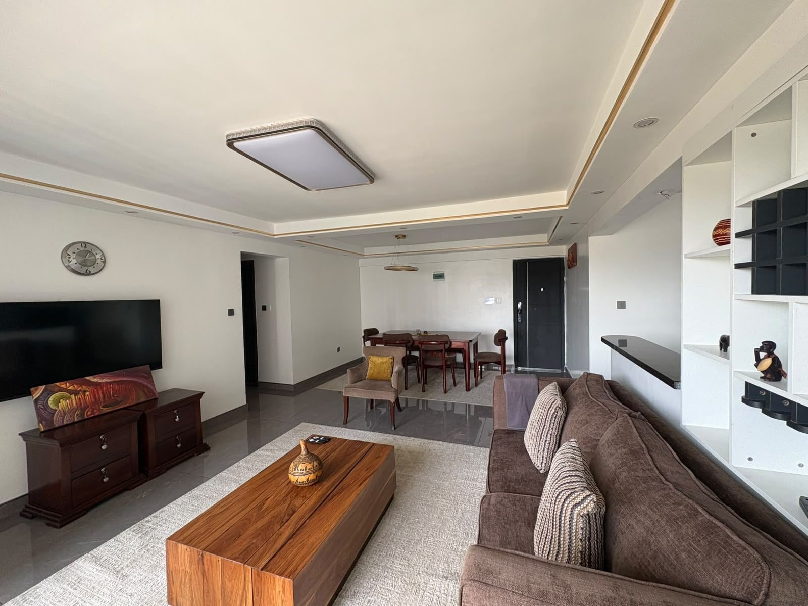 Ein modernes Wohnzimmer mit einem Flachbildfernseher, einem Holztisch, einem braunen Sofa und einem Essbereich mit Tisch und Stühlen.
