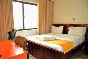 A hotel room with a wooden bed, a desk, and a chair. - Spacious 3-bedroom family apartment in beautiful Nairobi with AC and gym (Nairobi)