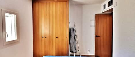 A bedroom with a bed, wooden wardrobe, ceiling fan, and a window.