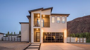 Une maison moderne à deux étages, dotée d’un garage, d’un balcon et offrant une vue sur un paysage montagneux.