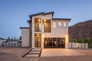 A modern two-story house with a garage, a balcony, and a view of a mountainous landscape. - Luxury Moab Oasis Pool, Spa & Fire Pit (Moab)