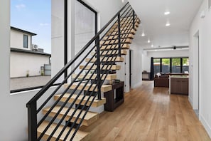 Un interior moderno con una escalera de madera, una zona de cocina y vistas por un amplio ventanal.