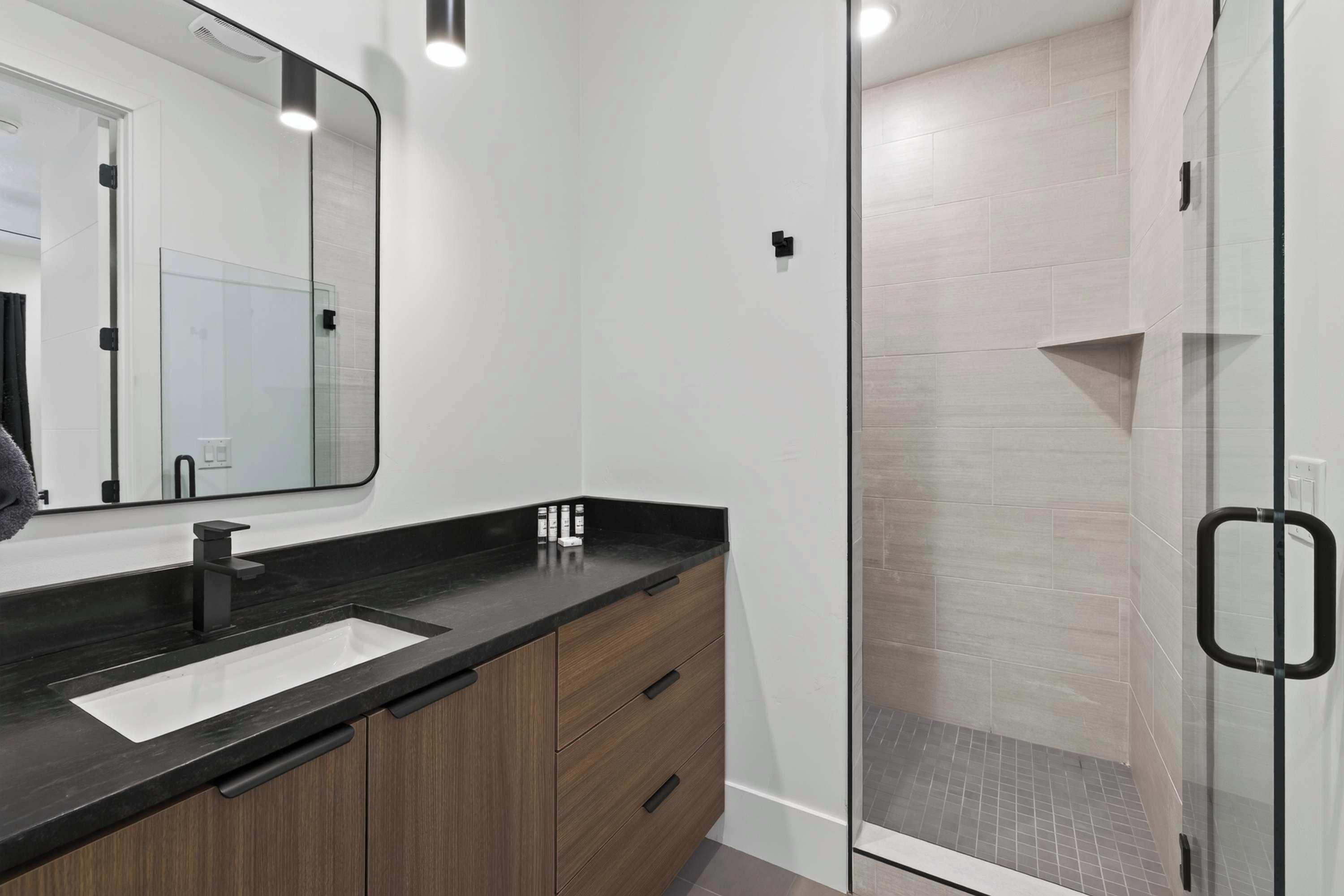A modern bathroom with a glass shower enclosure, a black countertop, and wooden cabinetry.