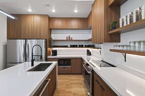 A modern kitchen with wooden cabinets, stainless steel appliances, and a white countertop. - Luxury Moab Oasis Pool, Spa & Fire Pit (Moab)